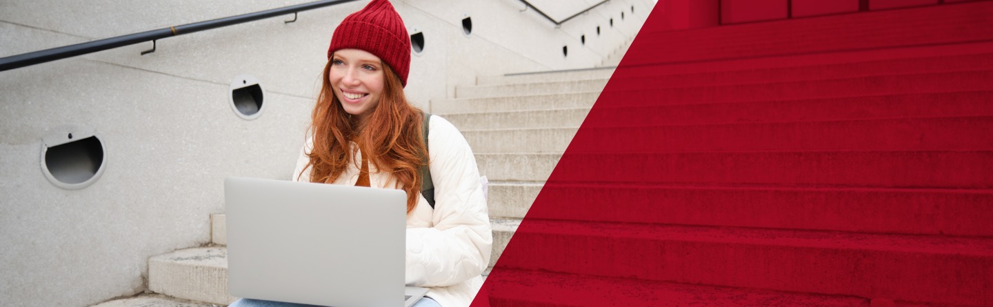 Ein junge Frau mit roter Mütze und Notebook auf Treppe