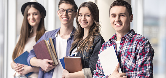 Vier junge Menschen mit Büchern und Heften stehen nebeneinander und lächeln in die Kamera.