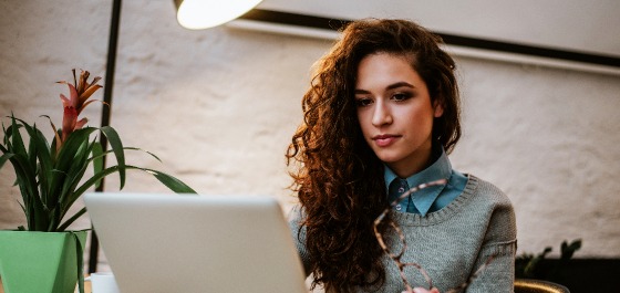 Junge Frau mit lockigen braunen Haaren sitzt vor einem Laptop.