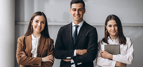 Zwei junge Frauen und ein junger Mann in Businesskleidung stehen nebeneinander und lächeln selbstbewusst in die Kamera.