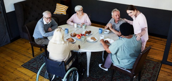 Mehrere alte Menschen an einem Tisch im Gespräch mit einer Pflegerin.