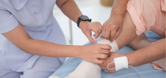 Eine Pflegekraft behandelt die Wunde am Bein einer älteren Dame