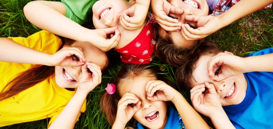 Quereinstieg in die Kinderbetreuung Kinder die am Boden liegen und eine Brille formen.