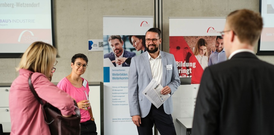 Ein Mann im grauen Anzug stellt 3 Referenten einem Publikum vor, einen Herrn und 2 Damen