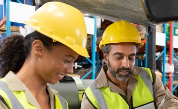 Eine farbige Frau mit Helm und ein arabischer Mann mit Helm unterhalten sich 