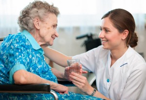 Junge Frau kümmert sich um eine ältere Dame im Pflegeheim und hält Ihre Hände 