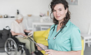 Pflegedienstleiterin mit älterem Patienten im Rollstuhl im Hintergrund.